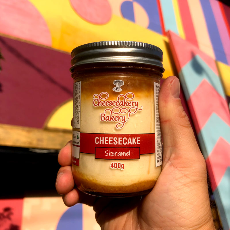 a jar of cheesecake is held up in front of a bright pink and yellow background